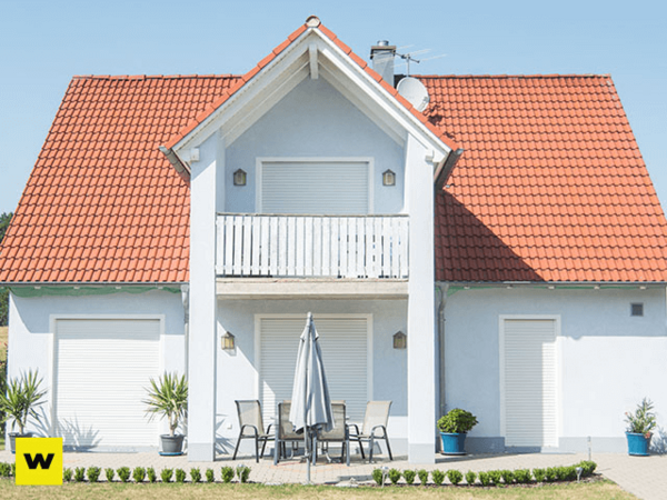 Modernes Einfamilienhaus mit rotem Satteldach, Rollläden und sonniger Terrasse.
